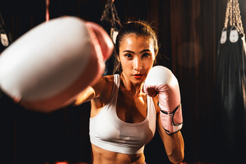 Asian female Muay Thai boxer punch fist in front of camera in ready to fight stance posing at gym...