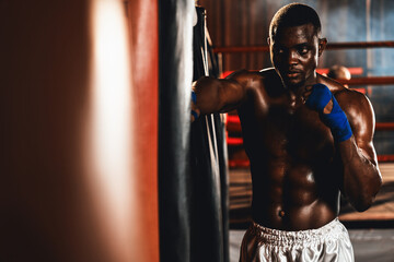 Fototapeta na wymiar African American Black boxer punching kicking bag as boxing bag training equipment in the gym for strength and stamina training for professional boxing match. Impetus