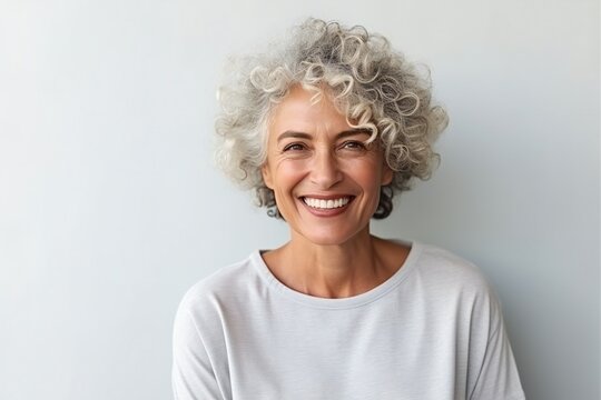 Stylish confident adult 60 years old femal standing smiling looking at camera at light background. Empty space banner Portrait of sophisticated grey hair woman advertising products and services.