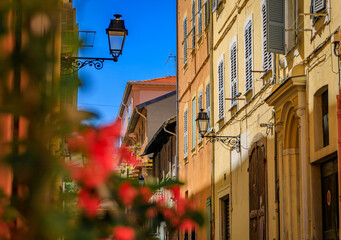 Picturesque narrow streets with colorful traditional houses in the old town of Menton, French Riviera, South of France, red flowers in the foreground