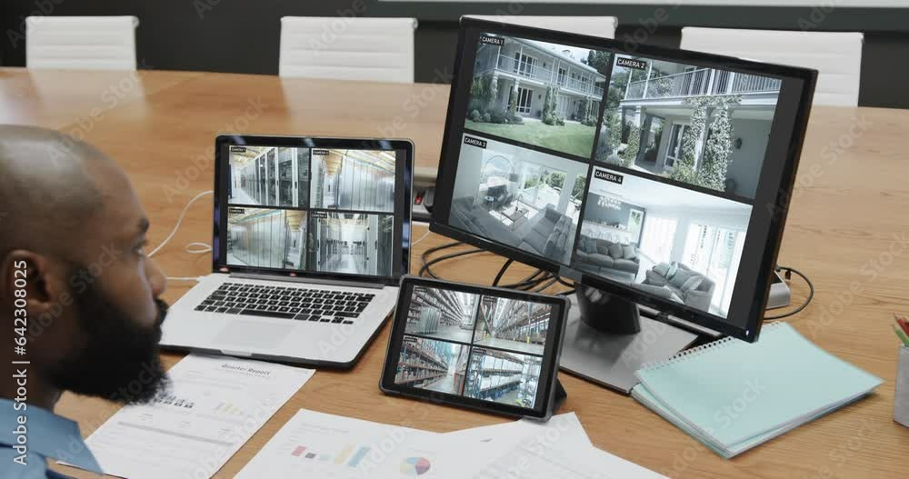 Wall mural African american male security officer watching cctv camera views on computer screens, slow motion