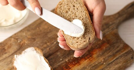 Spreading cheese or butter spread on bread. Female hands put a spread on a piece of bread with a knife on a cutting board. Making a sandwich.