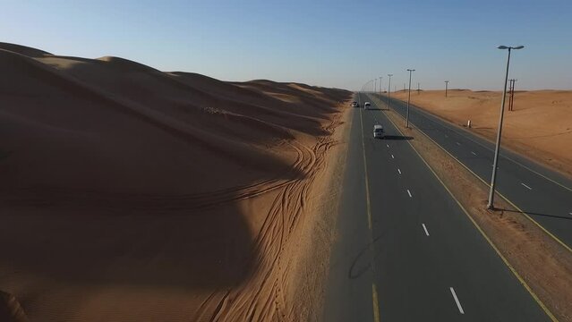 White car moves towards the camera on the desert highway. White Chrysler moves towards the quadcopter. The a quadcopter flies to the side and shots the desert and the sun.