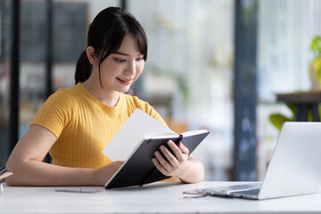 Naklejka premium Portrait of a young Asian woman reading a book in a library.