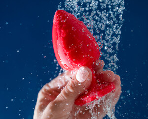 Woman washing red anal plug under shower on blue background. 