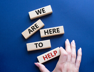 We are here to help symbol. Concept words we are here to help on wooden blocks. Beautiful deep blue background. Businessman hand. Business and we are here to help concept. Copy space.