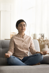 Peaceful young Indian yogi woman training focus, concentration, meditating sofa on short break,...