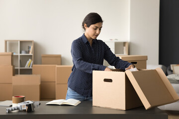 Pretty young Indian small business owner managing Internet shop, packing open box with purchase for sending, transportation, doing logistic job, working in commercial storage room