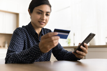 Positive Indian bank customer woman using Internet bank application on smartphone for paying by credit card on online shop, web store sale, using digital device for financial transaction