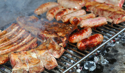 metal grill of the outdoor barbecue and sausages and pork ribs cooked over the glowing embers
