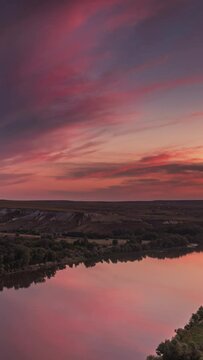 Scarlet sunset with fluffy clouds over a calm mirror river and chalk hills.