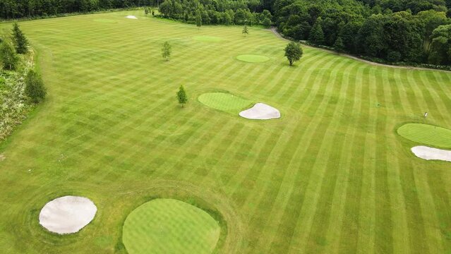 Golf course with its components teeing ground, rough, out of bounds, sand bunker, fairway, putting green, flagstick and hole with a green lawn and several players during the game