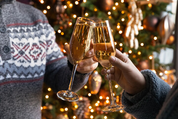 Close up young family couple clinking glasses with champagne or white wine with blurred festive Christmas tree on background, celebrating New Year winter December holidays, toasting congratulating.