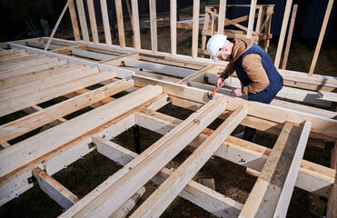 Man worker building wooden frame house on pile foundation. Carpenter hammering nail into wooden joist, using hammer. Carpentry concept.