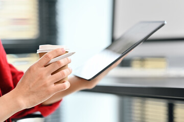 Closeup view of business man holding paper cup and using digital tablet at office desk