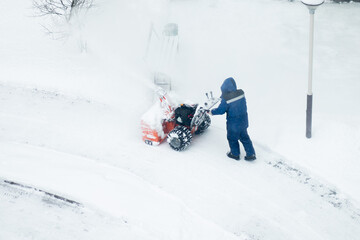 cleaning snow in the yard in winter, a janitor with a snowblower cleans the street