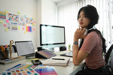 Pretty young creative woman listening to music in headphone and working on project at office desk