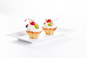 Beautiful cream cakes with cherries and grapes on a plate on a white background