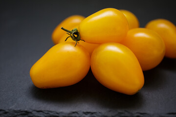 Yellow tomato. Tomatoes on a dark background. Bright yellow cherry tomatoes with green twigs