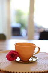 Cup of hot drink and red rose on table indoors