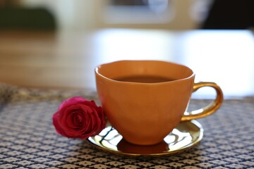 Cup of hot drink and red rose on table indoors, closeup