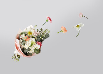 Different flowers flying to beautiful bouquet on grey background