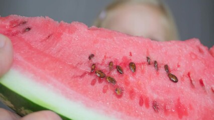 The girl reaches out her hands to the camera, takes a slice of watermelon and eats it. Close-up of a girl eating a watermelon.