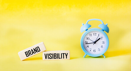 Brand visibility symbol. Wooden blocks with words.Yellow background with a clock. Copy space.