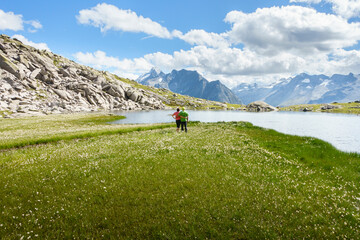 Ein idyllischer Bergsee inmitten der Alpen eingebettet in ein Meer aus Wollgras mit zwei Wanderern
