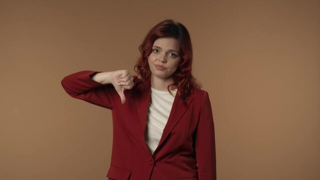 Medium isolated video of a young woman looking at the camera and giving thumbs-down to show her disagreement, complaint about something.