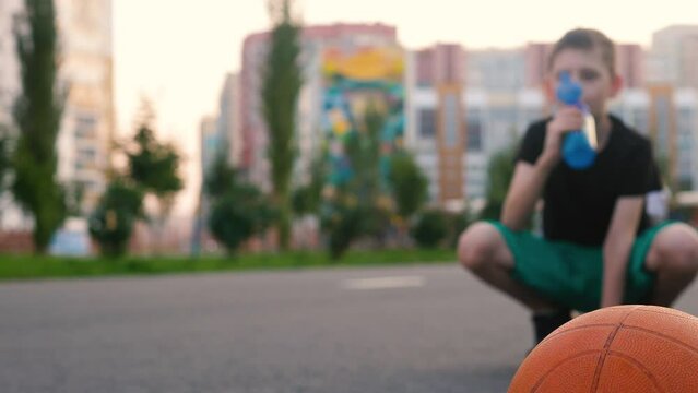 boy basketball player drinks water after playing sports. selective focus. basketball ball and breathing boy sportsman on the street drinking water