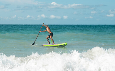 athletic wiry surfer guy swims with a paddle on a sup board in the sea