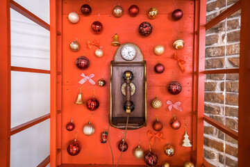 Red retro phone box with vintage wooden telephone is decorated with Christmas balls. New Year holiday background.