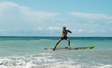 athletic wiry surfer guy swims with a paddle on a sup board in the sea