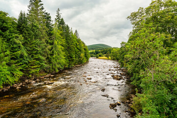 Fototapeta na wymiar Green mountain landscape with a river flowing between tall trees in the highlands of Scotland, UK.