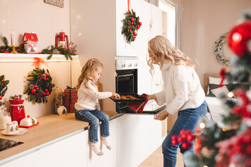 Young mother bake christmas cookies in decorated kitchen at home together. Motherhood. Winter holiday season.