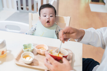 パパに離乳食を食べさせてもらってご機嫌な生後8か月の赤ちゃん	