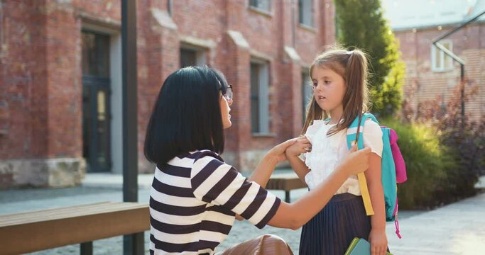 First day of school. Happy family concept. Back to school. Mother preparing and caring girl before leaving school at street. Young attractive woman talking to her daughter that running to class in
