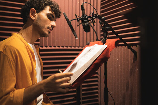 Thoughtful young ethnic man sitting and reading papers on desk in studio