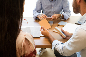 Unrecognizable men and woman sitting at table and checking wooden sample pieces in daylight