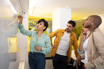 Happy diverse team members at writing board with woman manager sticking notes