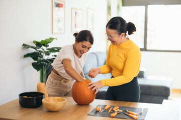 Happy ethnic young women standing with orange pumpkin at home