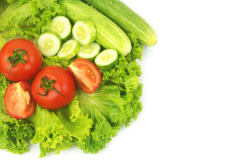 Fresh cucumbers and tomatoes on salad leaves background isolated on white.