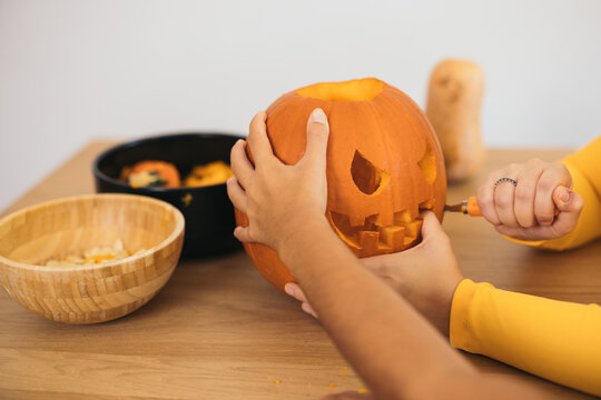 Unrecognizable women standing near table and preparing Halloween pumpkin