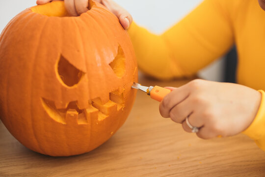 Unrecognizable woman sitting at table and carving Halloween pumpkin in daylight