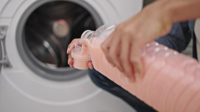 Young hispanic man washing clothes pouring detergent on washing machine at laundry room