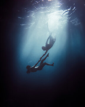 Unrecognizable couple in snorkel diving together in blue water