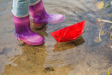  happy child girl in a yellow raincoat and paper boat at the river in autumn on nature.