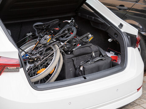 Parked white car with opened trunk with folded bicycle and briefcase in daylight