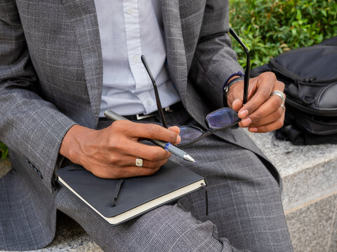 Faceless elegant guy sitting on street with notepad